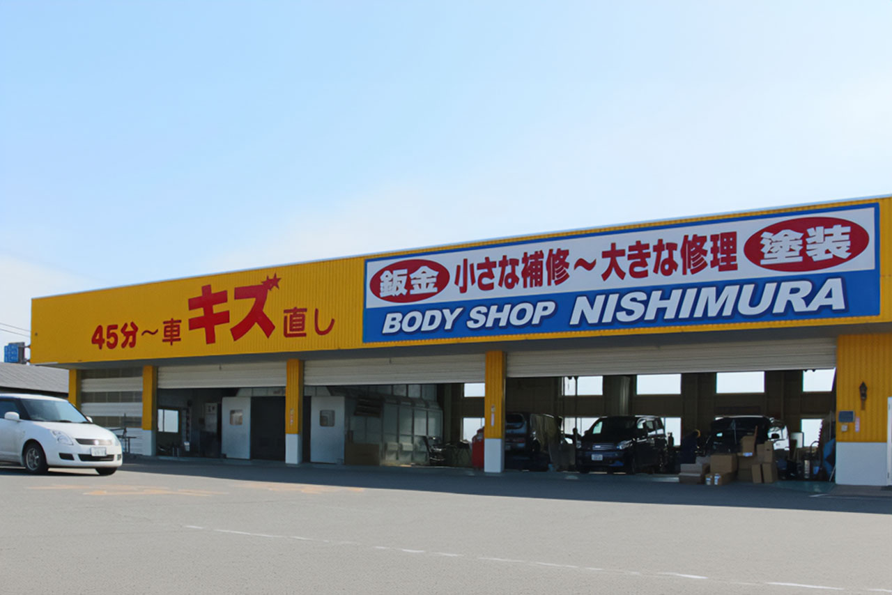 BODY SHOP NISHIMURAの大きな看板が掲げられた黄色の鈑金工場の建物外観