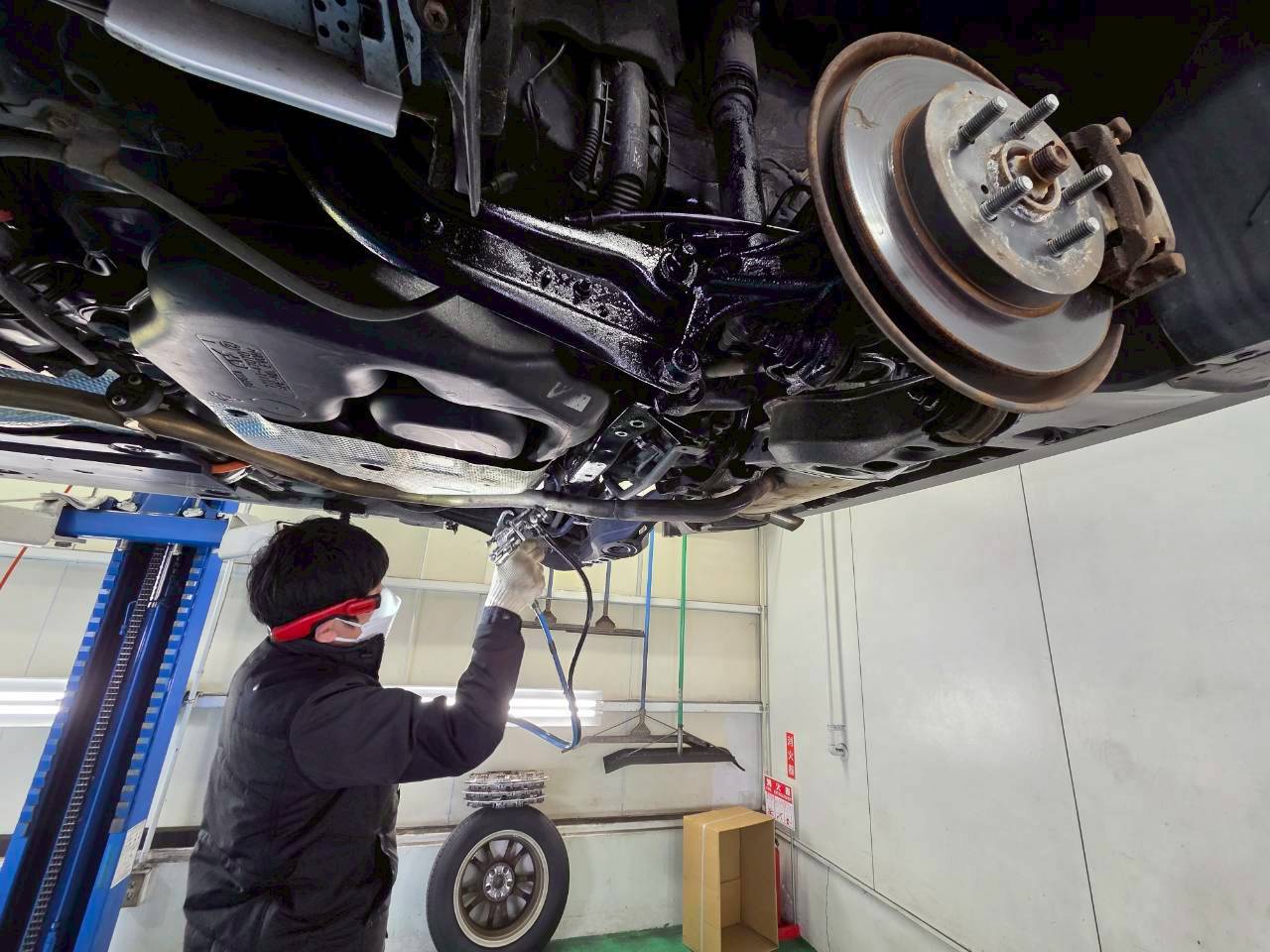 リフトアップされた自動車の床下に、作業員がスプレーガンで防錆塗料を吹き付けている様子